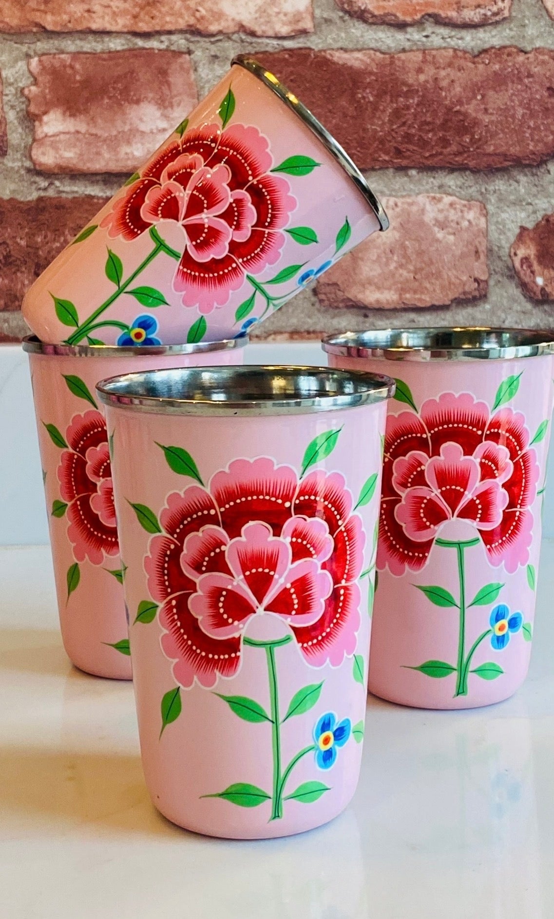 The Bamboo Bird set of four pink stainless steel tumblers featuring hand-painted red floral designs from Kashmir.