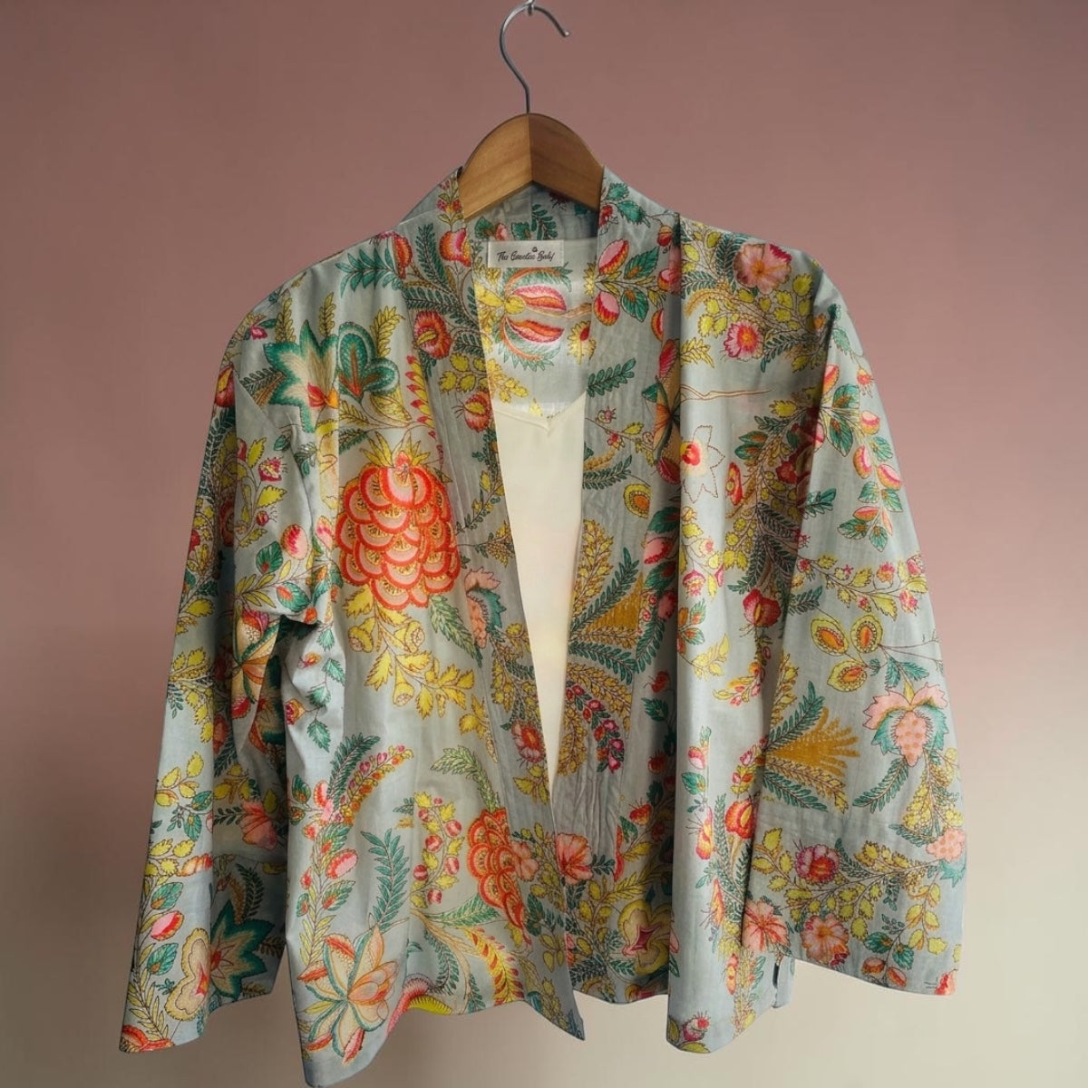 Pale blue kimono jacket on a wooden hangar with a pink background