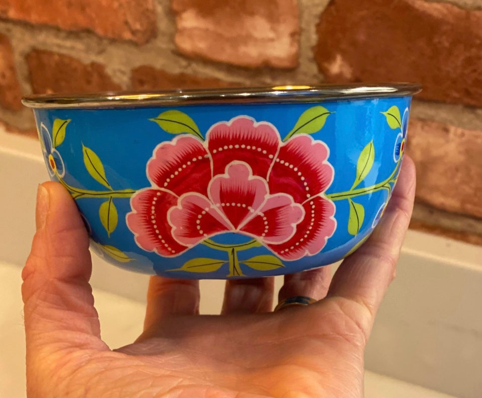 Hand holding a blue bowl with floral design against a brick wall background