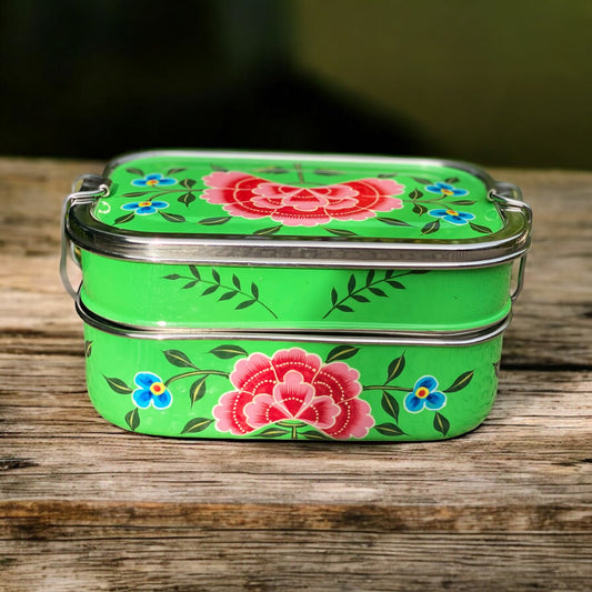 Green metal lunch box with floral design on a wooden surface