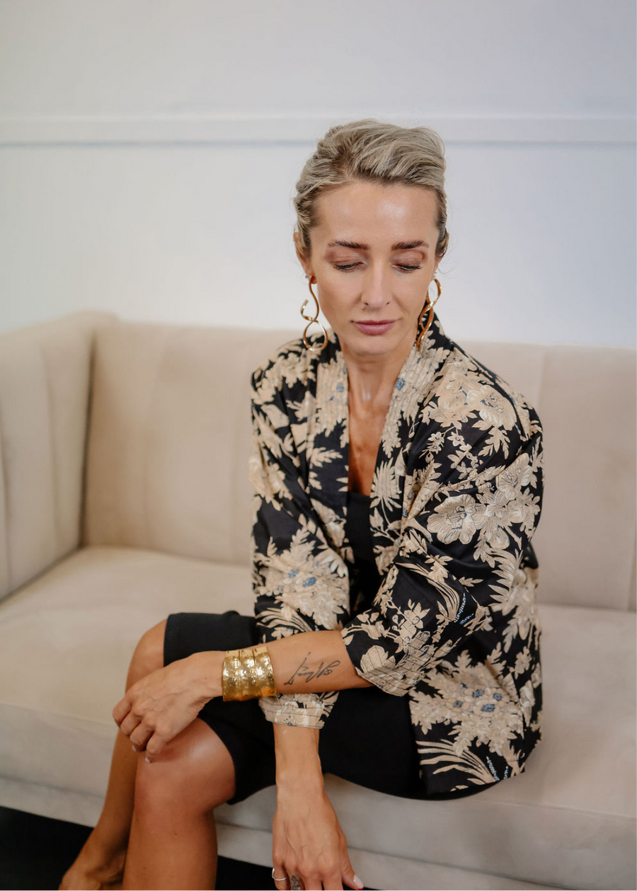 Woman sitting on a couch wearing a black and beige floral jacket