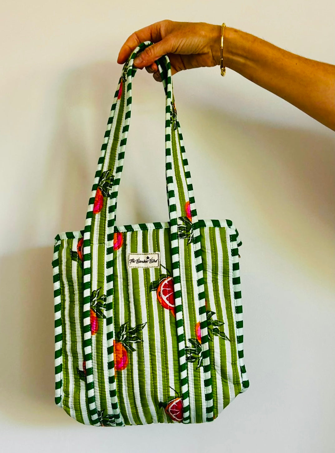 A hand holding a green and white striped fabric tote bag with red strawberry prints and a white brand label that reads 'My Sweet Spot'.