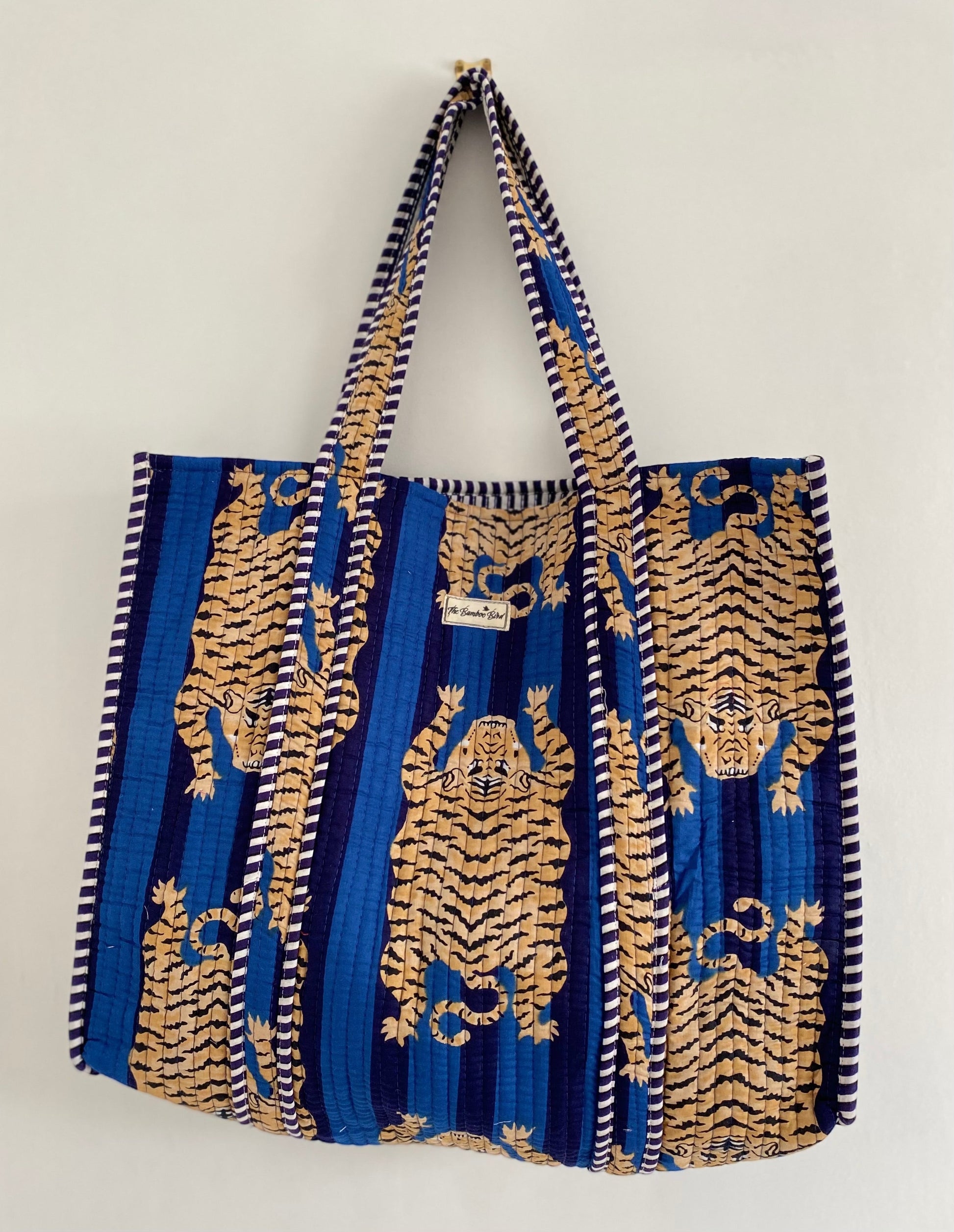 The Bamboo Bird blue quilted cotton tote bag featuring a hand block-printed tiger pattern and striped shoulder straps.