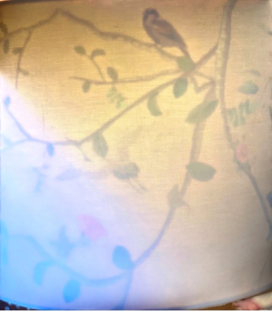 The Bamboo Bird cream linen drum lampshade illuminated to reveal a gold chinoiserie bird and botanical interior pattern