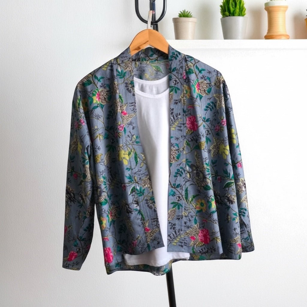The Bamboo Bird dusky blue cotton kimono jacket featuring a bird and floral Chinoiserie print on a hanger.