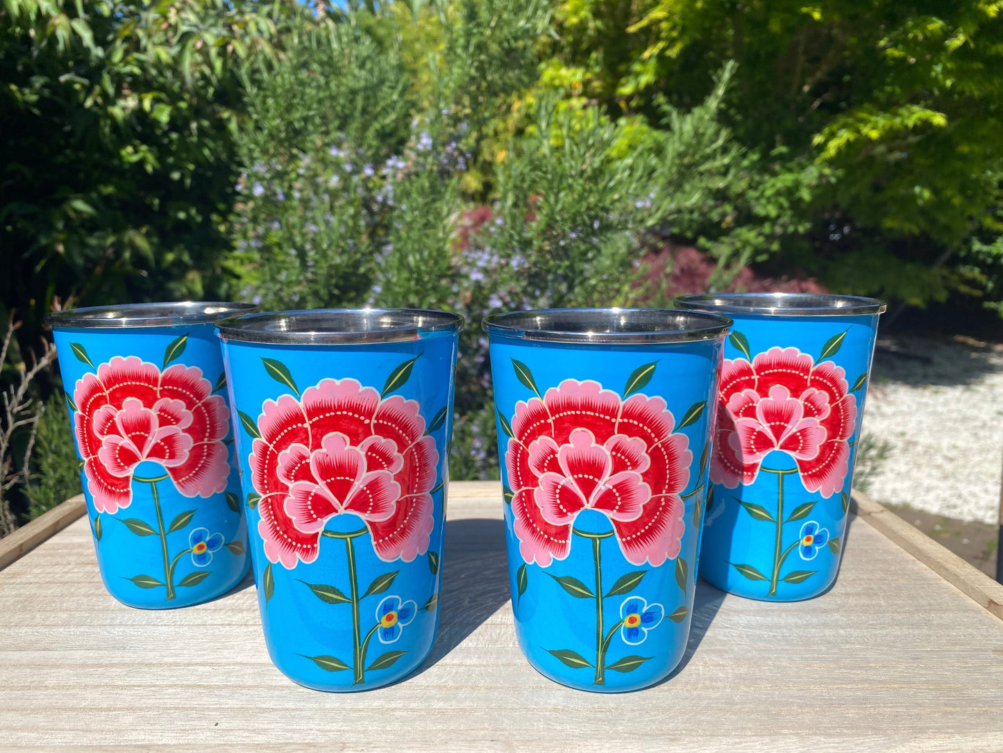 The Bamboo Bird set of four blue stainless steel tumblers featuring hand-painted red floral designs from Kashmir.