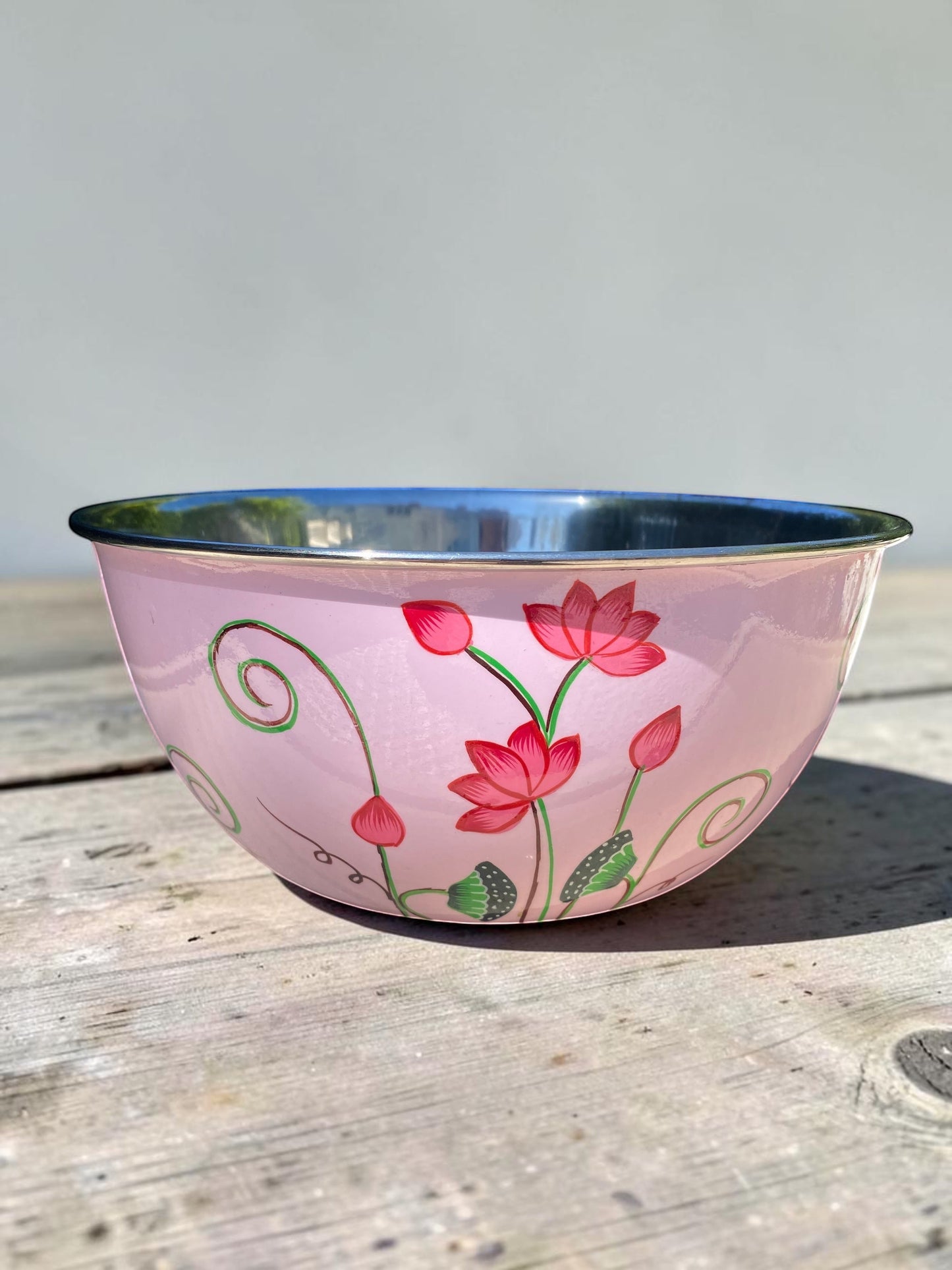 The Bamboo Bird hand-painted pink stainless steel and enamel bowl with floral lotus design on a wooden surface.